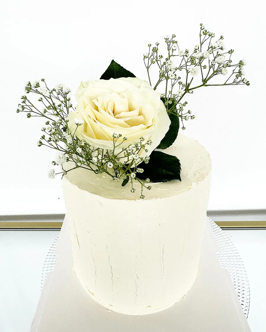 Gâteau blanc surmonté d'une rose blanche et de gypsophile, pour des fiançailles