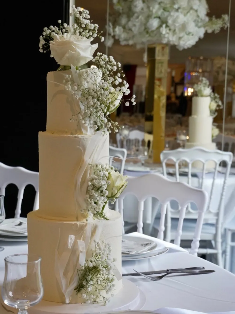 Pièce montée de trois étages, ton ivoire, roses blanches fraîches et gypsophile, sur une table de réception